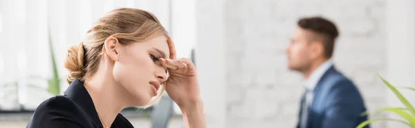 Exhausted businesswoman with hand near eyes looking down with blurred colleague on background, banner — Stock Photo