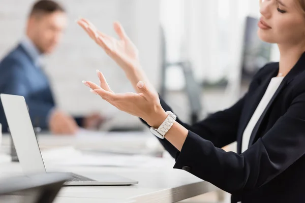 Vista ritagliata di triste gestualità donna d'affari, mentre seduto vicino al computer portatile sul posto di lavoro su sfondo sfocato — Stock Photo