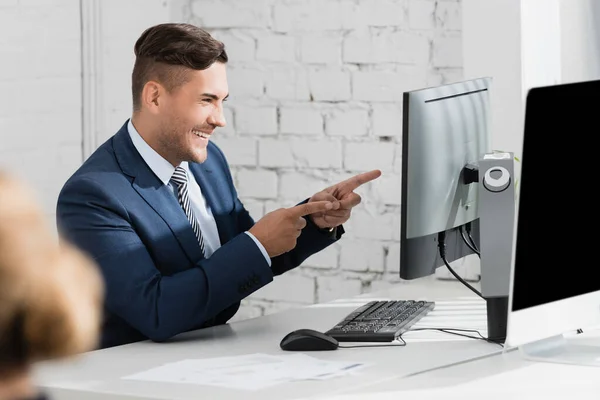 Allegro uomo d'affari che punta con le dita mentre guarda il computer portatile sul posto di lavoro in primo piano sfocato — Foto stock