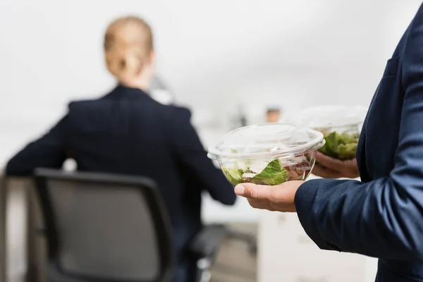Empresário segurando tigelas de plástico com alimentos, enquanto estava perto colega sobre fundo borrado — Fotografia de Stock