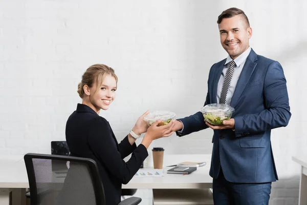 Lächelnde Geschäftsleute mit Essen in Plastikschüsseln, in der Pause in die Kamera guckend — Stockfoto