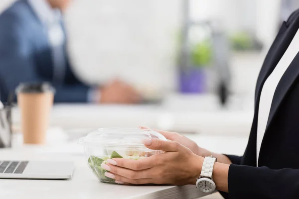Ausgeschnittene Ansicht einer weiblichen Führungskraft mit Plastikschüssel und Mahlzeit am Arbeitsplatz auf verschwommenem Hintergrund — Stockfoto