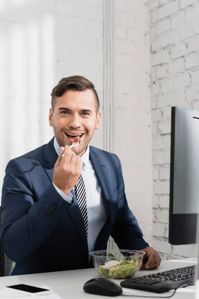 Smiling businessman looking at camera, while eating meal from plastic bowl at workplace — Stock Photo