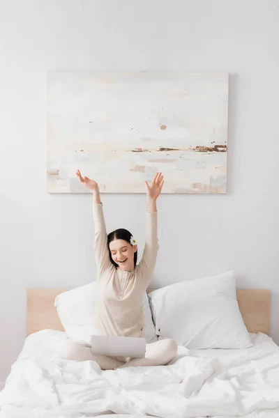 Amazed freelancer with vitiligo sitting with hands above head and looking at laptop in bedroom — Stock Photo