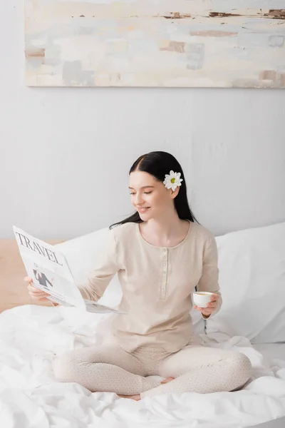 Glückliche Frau mit Blume im Haar hält Tasse und liest Reisezeitung — Stockfoto