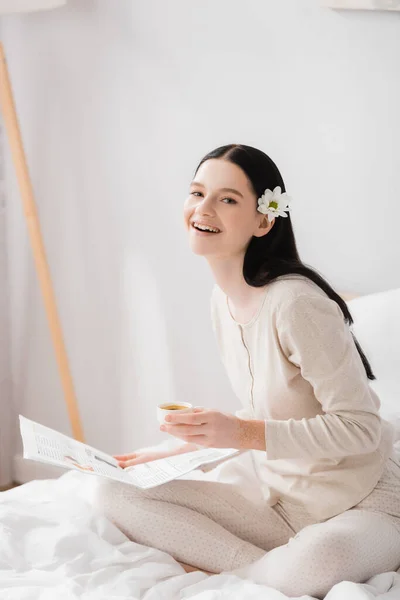 Mujer feliz con vitiligo y flor en la taza de la celebración del pelo y periódico - foto de stock