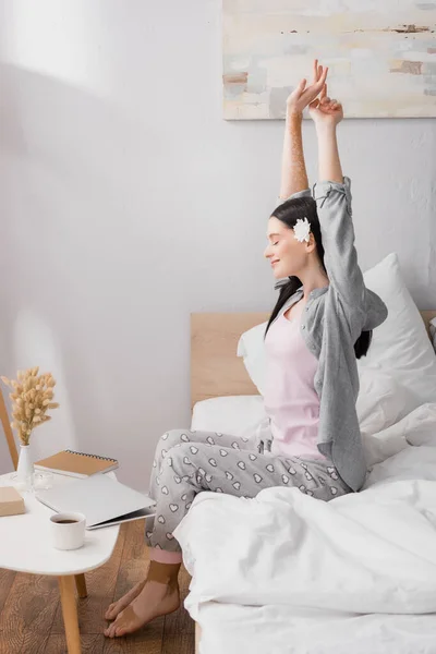Glückliche Frau mit Vitiligo und Blume im Haar Stretching im Schlafzimmer — Stockfoto