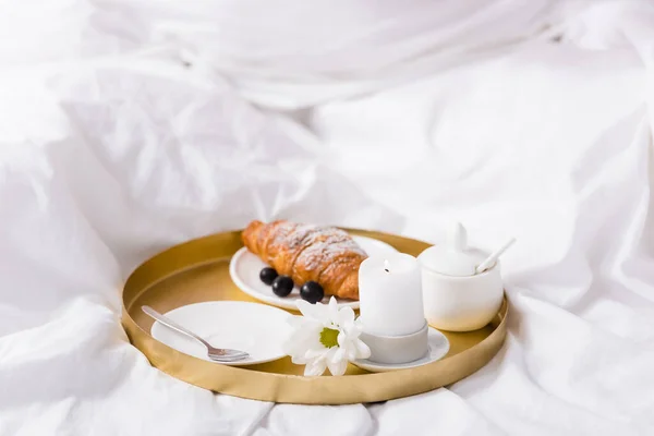 Croissant e uva vicino alla candela sul vassoio della colazione in camera da letto — Foto stock