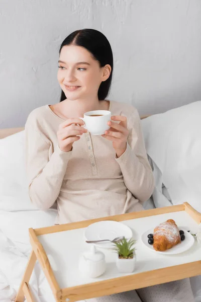 Young happy woman with vitiligo holding cup of tea near breakfast on tray — Stock Photo