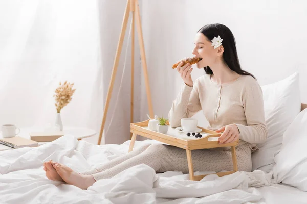 Young brunette woman with vitiligo eating croissant near breakfast tray — Stock Photo