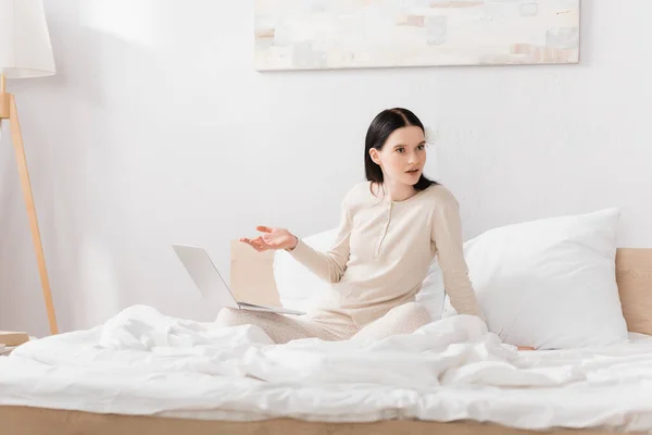 Displeased woman with vitiligo pointing with hand at laptop on bed — Stock Photo