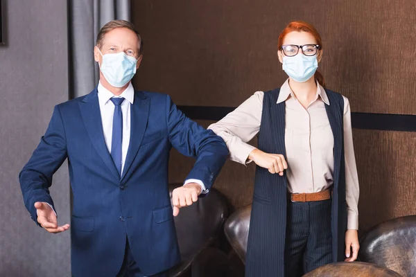 Empresarios con máscaras médicas mirando a la cámara mientras se saludan con los codos en la sala de reuniones - foto de stock