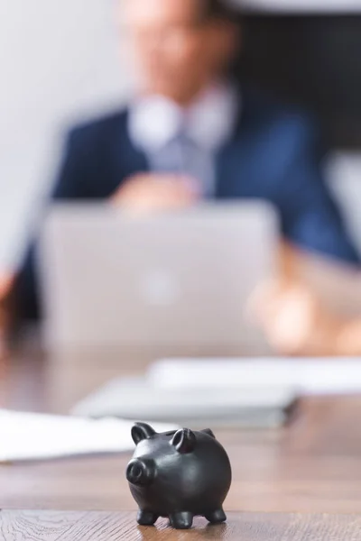 Petite tirelire noire sur table avec homme d'affaires flou sur fond — Photo de stock