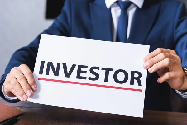 Cropped view of businessman holding sign with investor lettering in meeting room on blurred background — Stock Photo