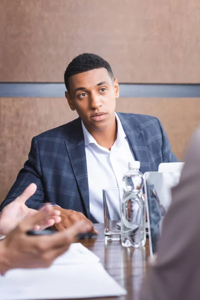 African american businessman sitting at workplace while looking at blurred colleague on foreground — Stock Photo