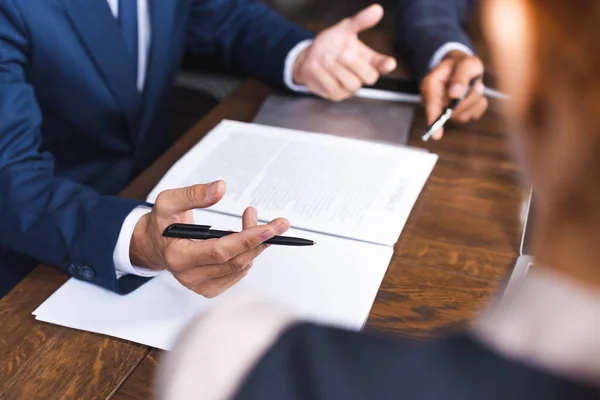 Cropped view of investor with pen gesturing near documents on workplace on blurred foreground — Stock Photo