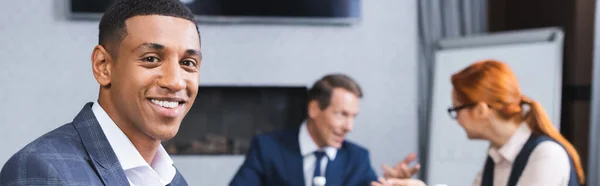 Sorrindo empresário afro-americano olhando para a câmera com colegas embaçados em segundo plano na sala de reuniões, banner — Fotografia de Stock