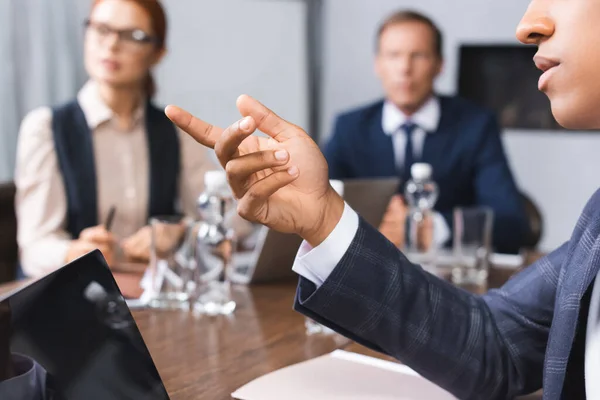 Крупный план африканского американского бизнесмена, указывающего пальцем на размытых коллег на заднем плане в зале заседаний — стоковое фото