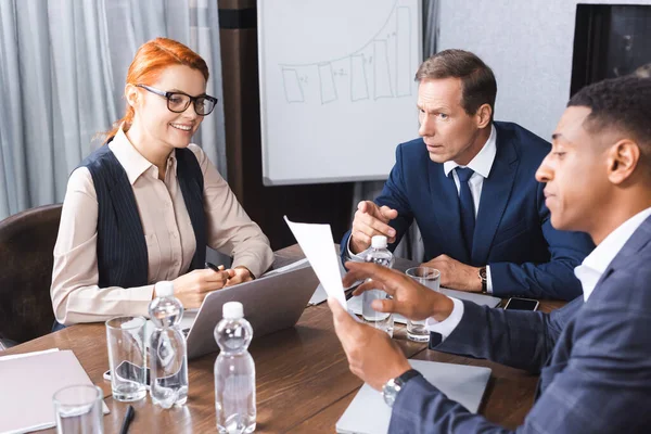 Serious executive pointing with finger at paper in hands of african american man while looking at businesswoman in boardroom — Stock Photo