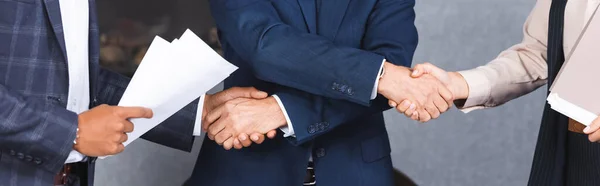 Vista recortada del hombre de negocios estrechando la mano con colegas multiculturales, pancarta - foto de stock