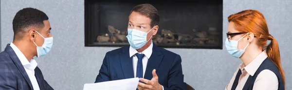 Мультикультурные бизнесмены в медицинских масках разговаривают во время деловой встречи в зале заседаний, баннер — стоковое фото