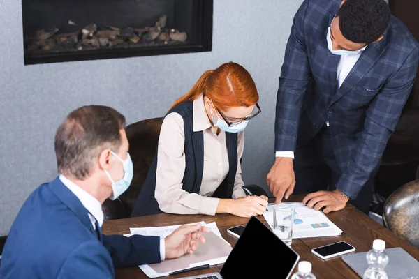 Redhead executivo escrevendo em documento perto de empresários multiculturais na sala de reuniões — Fotografia de Stock