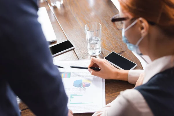 Redhead businesswoman pointing with pen at paper with charts near businessman at workplace on blurred foreground — Stock Photo