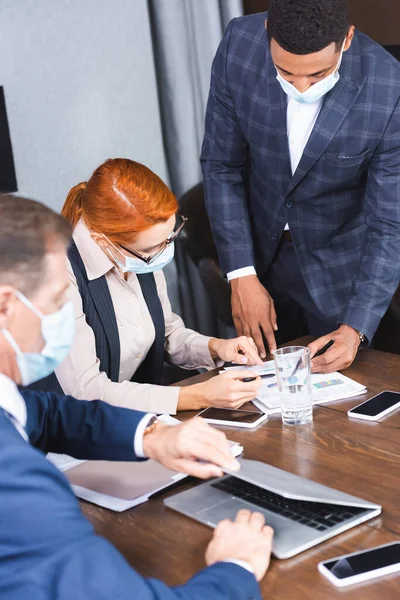 Multikulturelle Geschäftsleute zeigen mit Stiften auf Dokument am Arbeitsplatz im Sitzungssaal mit verschwommenem Kollegen im Vordergrund — Stockfoto