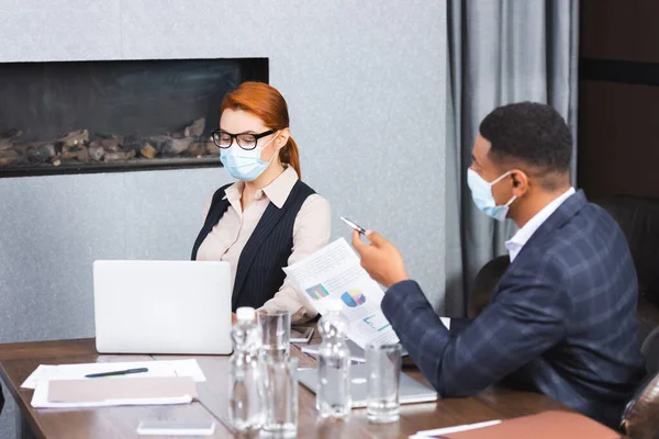 Hombre de negocios afroamericano con documento apuntando con pluma mientras está sentado cerca de la mujer de negocios en el lugar de trabajo - foto de stock