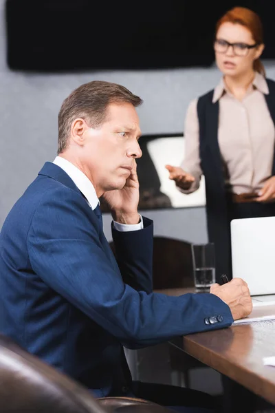 Homme d'affaires effrayé assis sur le lieu de travail avec un cadre en colère flou sur fond — Photo de stock