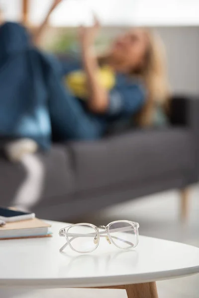 Eyeglasses on coffee table with blurred woman on background — Stock Photo