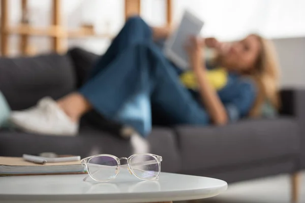 Eyeglasses on coffee table with blurred woman on background — Stock Photo