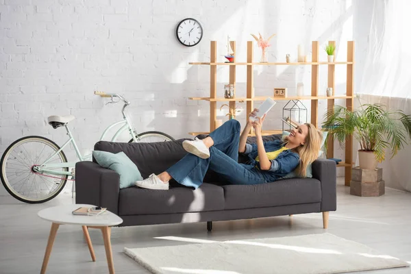 Full length of smiling woman looking at digital tablet while lying on couch at home — Stock Photo