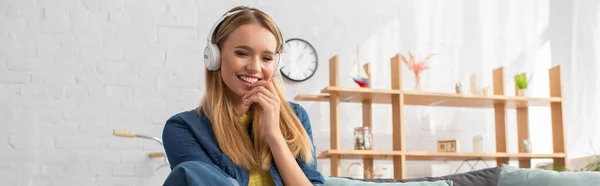 Весела молода блондинка в навушниках вдома на розмитому фоні, банер — стокове фото