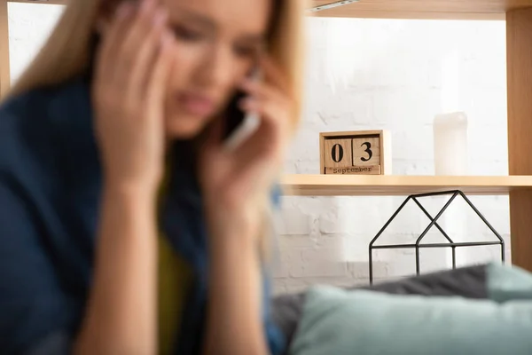 Calendario in legno sullo scaffale con donna preoccupata offuscata che parla sullo smartphone in primo piano — Foto stock