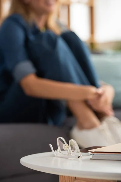 Brille auf Couchtisch mit verschwommener junger Frau im Hintergrund — Stockfoto