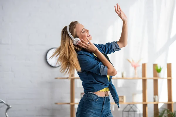 Fröhliche junge Frau mit Kopfhörern tanzt zu Hause auf verschwommenem Hintergrund — Stockfoto