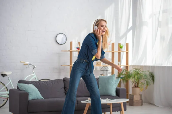 Heureuse femme blonde dans les écouteurs riant et regardant loin à la maison — Photo de stock