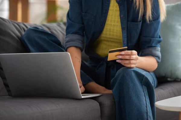 Обрізаний вид молодої жінки з кредитною карткою з ноутбуком на розмитому фоні — стокове фото