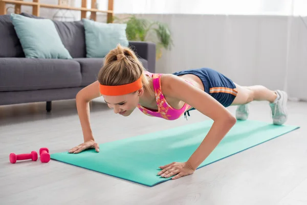 Comprimento total de sportswoman positivo fazendo press ups no tapete de fitness no fundo borrado — Fotografia de Stock