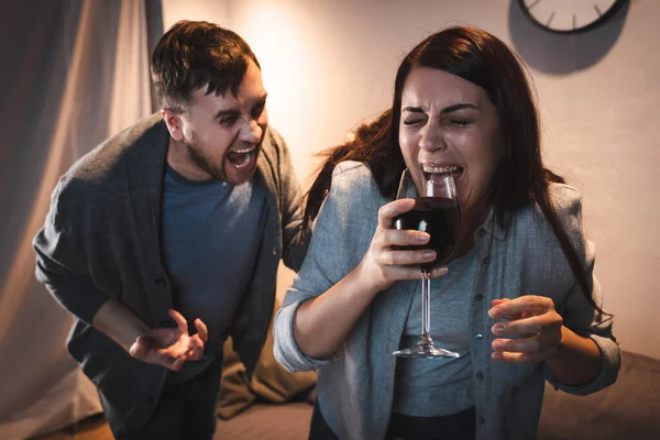 Bêbado homem gritando em álcool viciado esposa segurando copo de vinho com olhos fechados — Fotografia de Stock