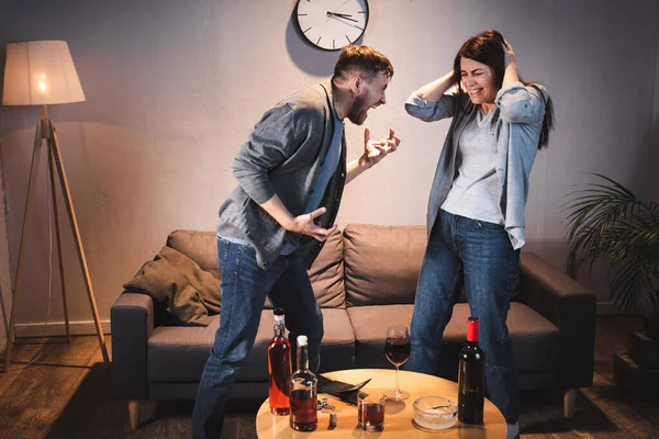 Couple ivre querelle près de la table avec des bouteilles d'alcool à la maison — Photo de stock