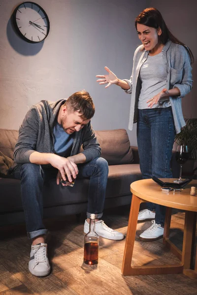 Aggressive Frau brüllt betrunkenen Mann an, der mit gesenktem Kopf auf Sofa sitzt — Stockfoto