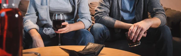 Vue recadrée du mari et de la femme assis avec des verres d'alcool près d'un portefeuille vide, avant-plan flou, bannière — Photo de stock