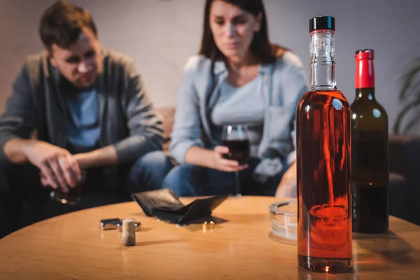 Bottles of alcohol and empty wallet on table near drunk couple on blurred background — Stock Photo