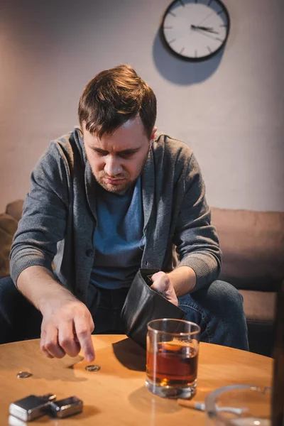 Homme ivre tenant portefeuille vide près de pièces de monnaie et verre de whisky au premier plan flou — Photo de stock