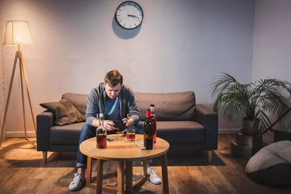 Uomo dipendente con portafoglio vuoto vicino a bottiglie di bevande alcoliche sul tavolo — Foto stock