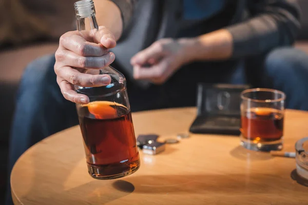 Visão parcial do homem viciado em álcool segurando garrafa de uísque, fundo embaçado — Fotografia de Stock