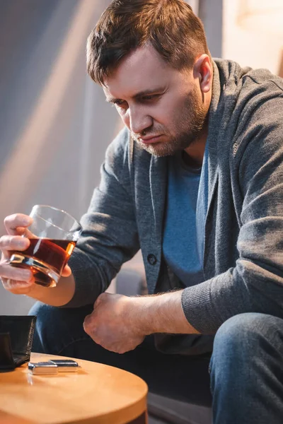 Homme frustré tenant un verre de whisky assis à la maison seul — Photo de stock