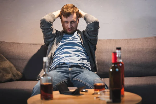 Drunk man sitting near table with alcohol drinks and empty wallet on blurred foreground — Stock Photo